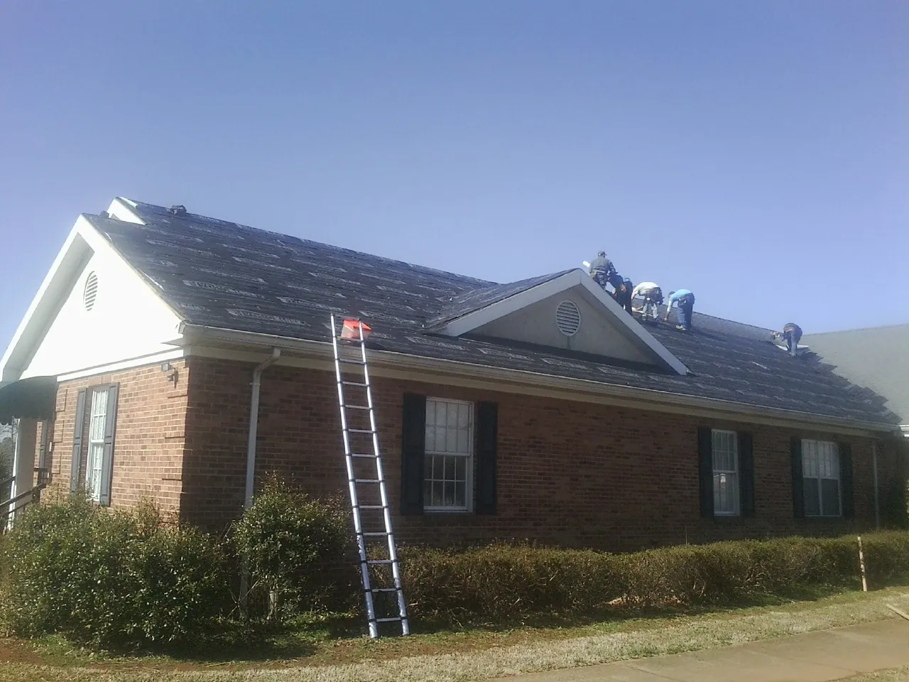 Crew tearing shingles off a brick ranch roof with a ladder set — Emergency Roof Repair work by our crew in Medimont