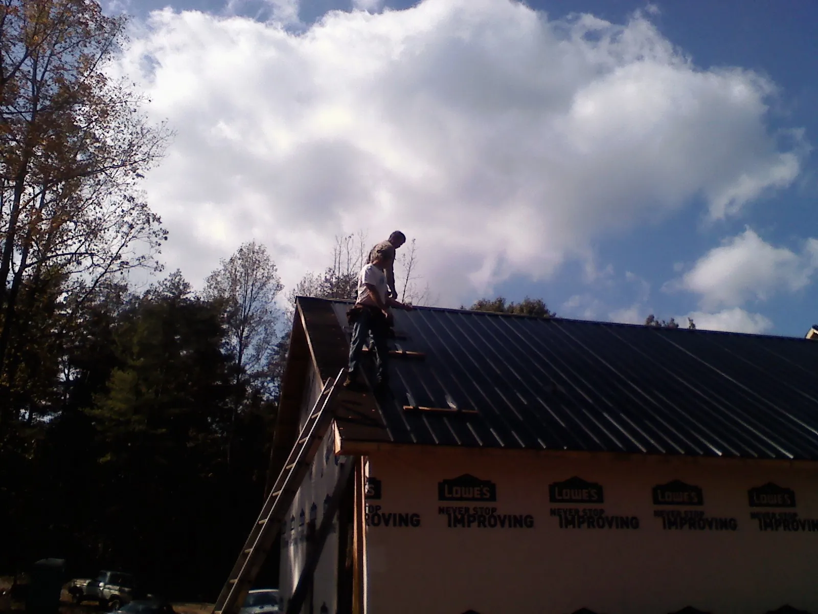 Roofer fastening dark metal panels high against a cloudy sky, from a Roof Inspection job in Medimont