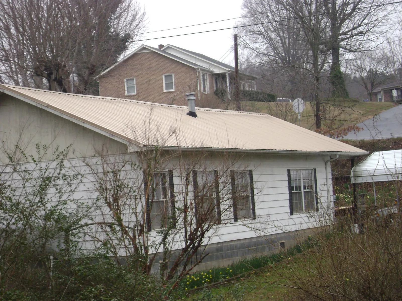 Tan metal roof on a white sided house set into a hillside — Commercial Roofing by Roofing Brothers in Medimont