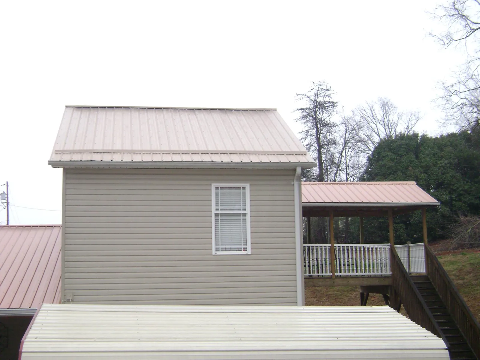 Tan metal roofs on a two story addition and attached porch, from a Roof Replacement job in Medimont